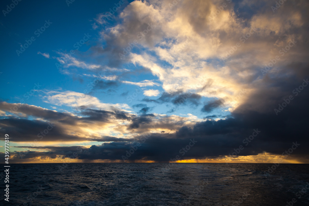 Sunbeams make their way through the cloudy sky, covered with clouds on the open sea at sunset.