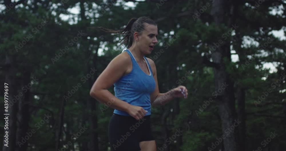 Slow motion tracking shot of a young woman in sportswear jogging through an evergreen forest on a country road on heavy rain. Slow motion tracking shot of a young woman in sportswear jogging through an evergreen forest on a country road on heavy rain.