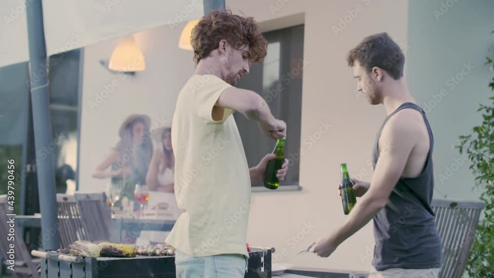 Group of friends preparing meat bbq. Men cheering with beer drink.Double couple of friends talking, drinking, laughing together in summertime.