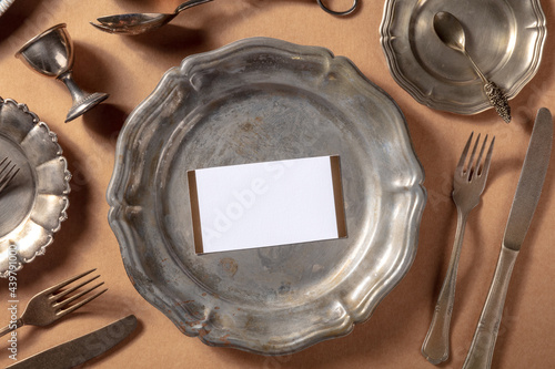 Dinner invitation mockup with an RSVP card, shot from the top on a vintage silver salver with other elegant tableware and cutlery, overhead flat lay mock up for a formal occasion