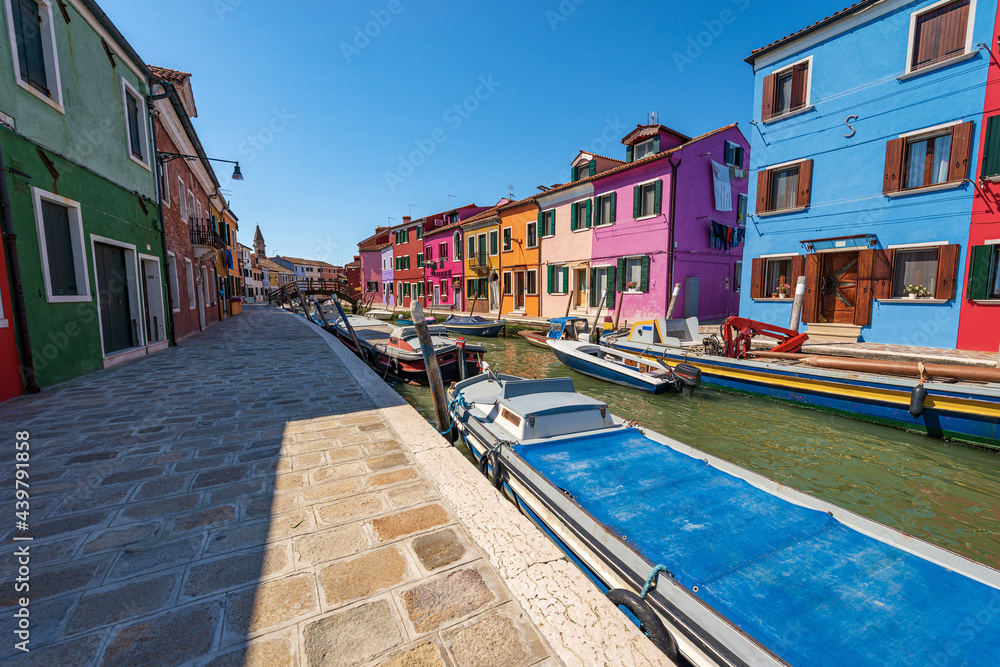 Burano island in the Venetian lagoon with multi colored houses (bright colors) and a canal with moored small boats in a sunny spring day. Venice, UNESCO world heritage site, Veneto, Italy, Europe.