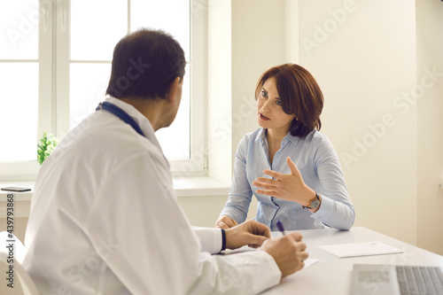 Mid-aged caucasian woman patient describing symptoms explaining health problem talking to male doctor asking for advice. Live medical consultation at clinic office. Medicine and professional help