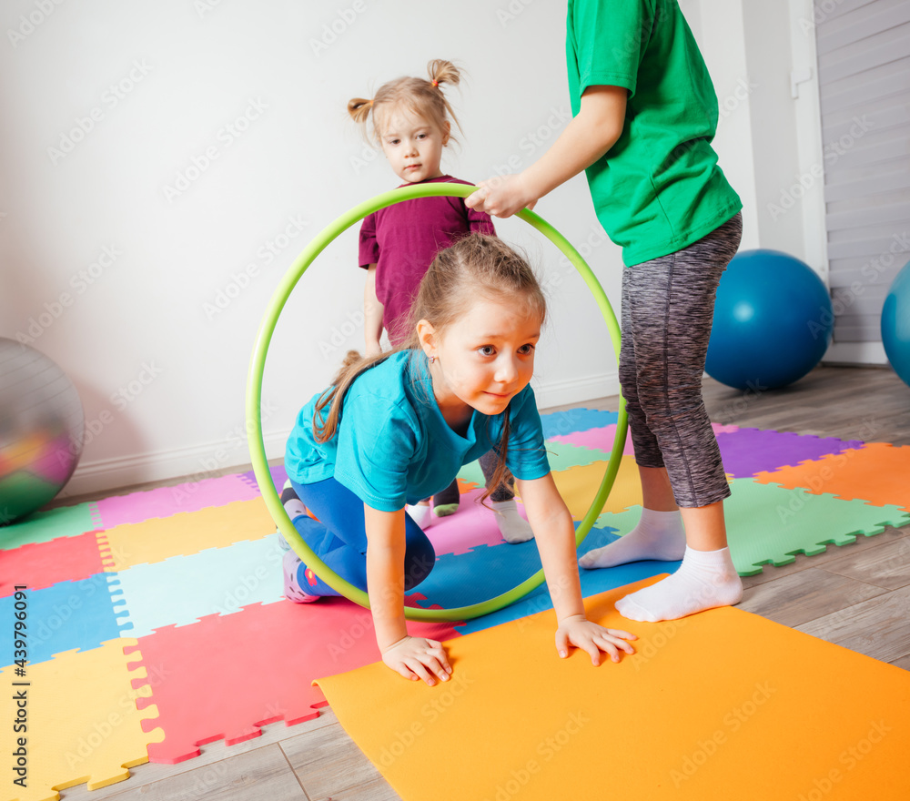 Fototapeta premium Curly girl crawling on colorful floor through hula hoops