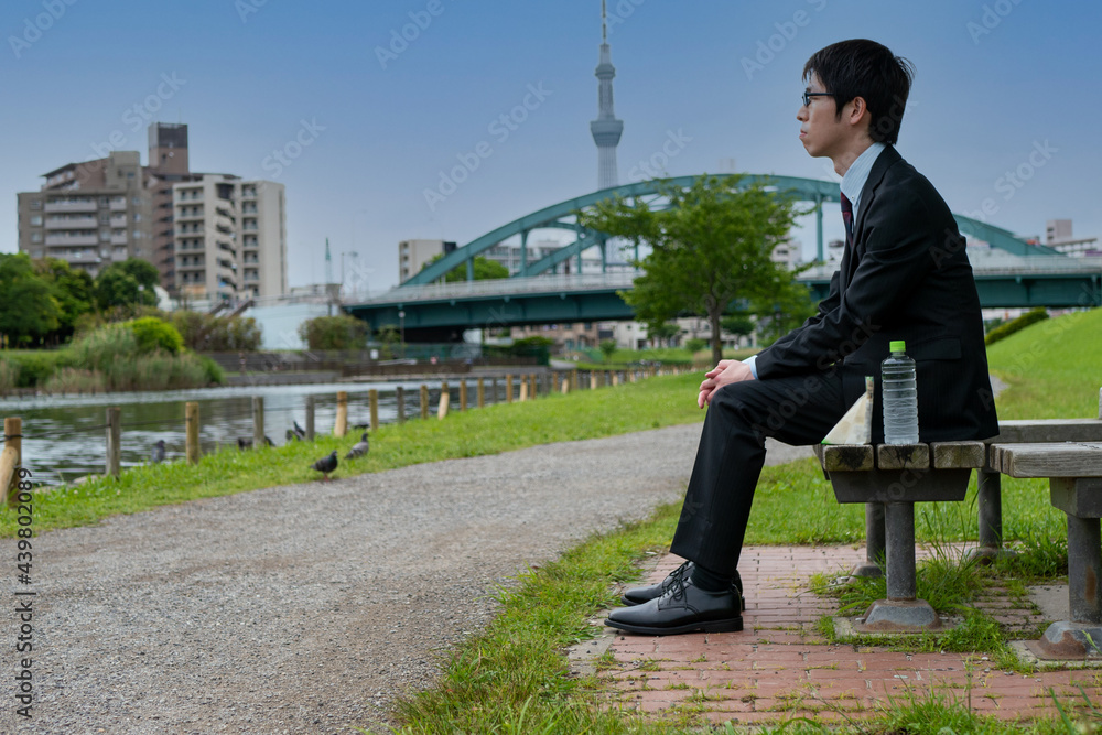 スカイツリーが見える公園でベンチに座る日本人男性