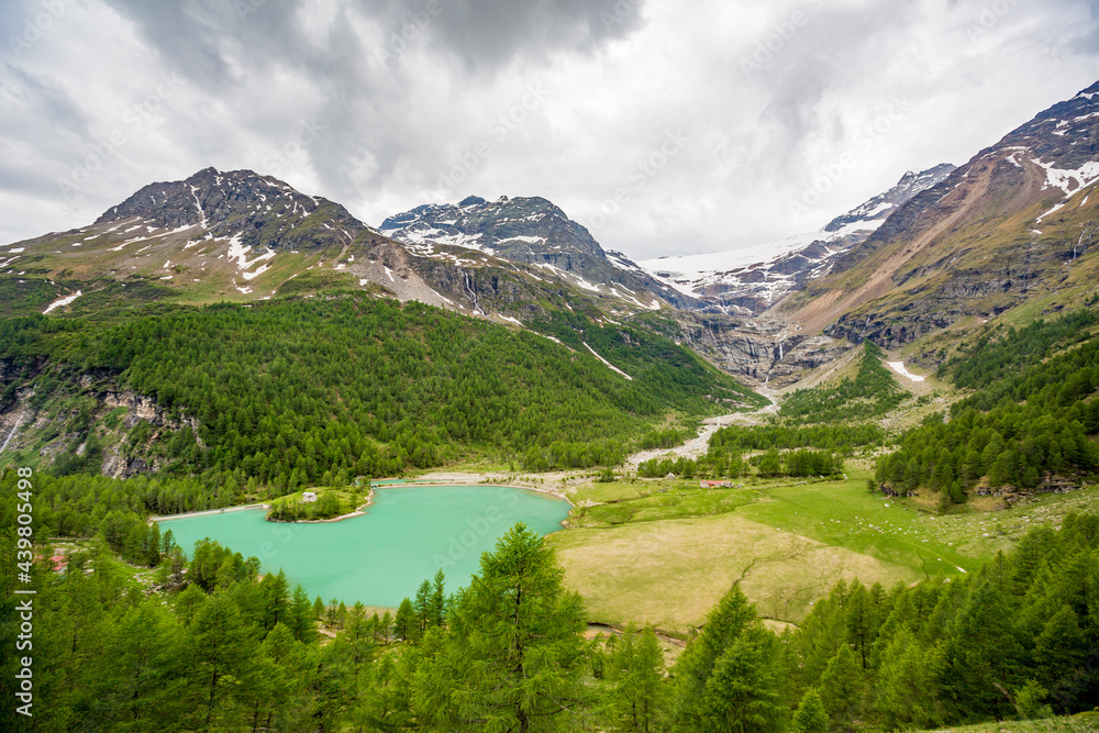 Scenery spring season perspective from Bernina Express red tourist train that goes high up in the Swiss Alps. Cloudy sky and green hills, crystal blue waters lake