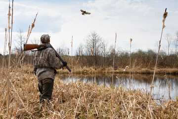 the hunter stands on the shore of the lake and looks at the flying duck