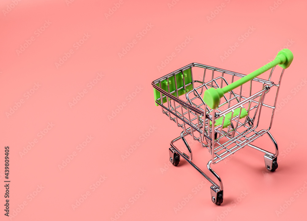 Empty miniature supermarket trolley on a colored background. The concept of buying and selling goods. Online sales on the Internet. Selective focus, copy space.
