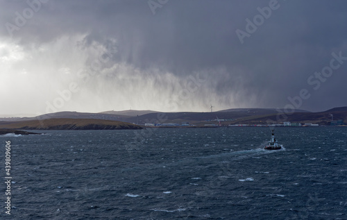The Pilot Boat Knab ahead of a Vessel approaching Bressay Sound in a Winters squall in the Shetland Islands with dark clouds above. photo