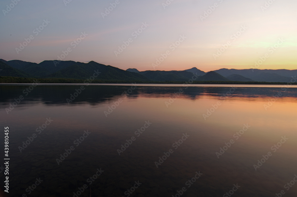 夕暮れの空に際立つ山々のシルエットを湖面に反射する湖。