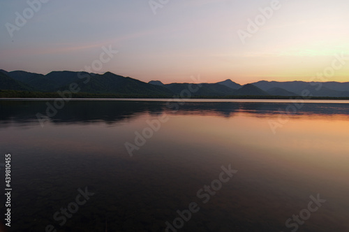 夕暮れの空に際立つ山々のシルエットを湖面に反射する湖。 © Masa Tsuchiya