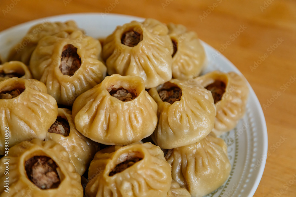 Steamed national Mongolian food dumpling Buuz filled with minced beef, white plate, wooden table, Close up east Siberian Buryats dish poses, Juicy minced meat wrapped handmade dough shirt above view Steamed national Mongolian food dumpling Buuz filled with minced beef, white plate, wooden table, Close up east Siberian Buryats dish poses, Juicy minced meat wrapped handmade dough shirt above view