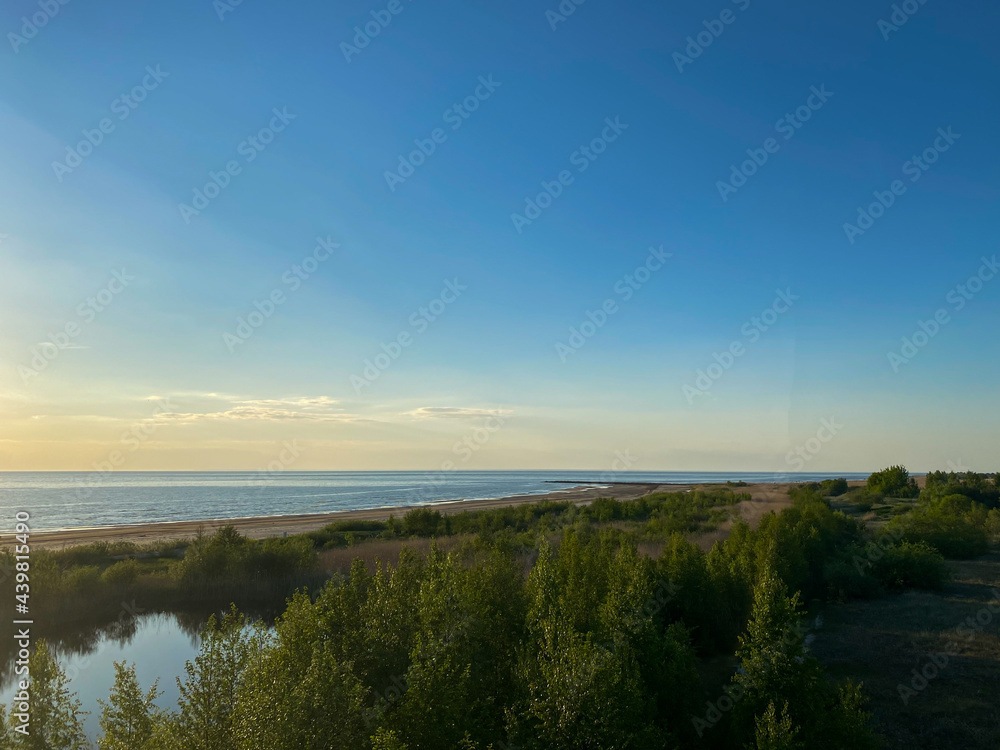 Aerial shot. Sea shore with green bushes in the summer evening with a sunset sky.