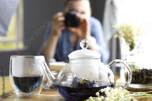 A woman photographs a teapot and tea in a glass. Photographer works. Photograph of a girl with a camera.