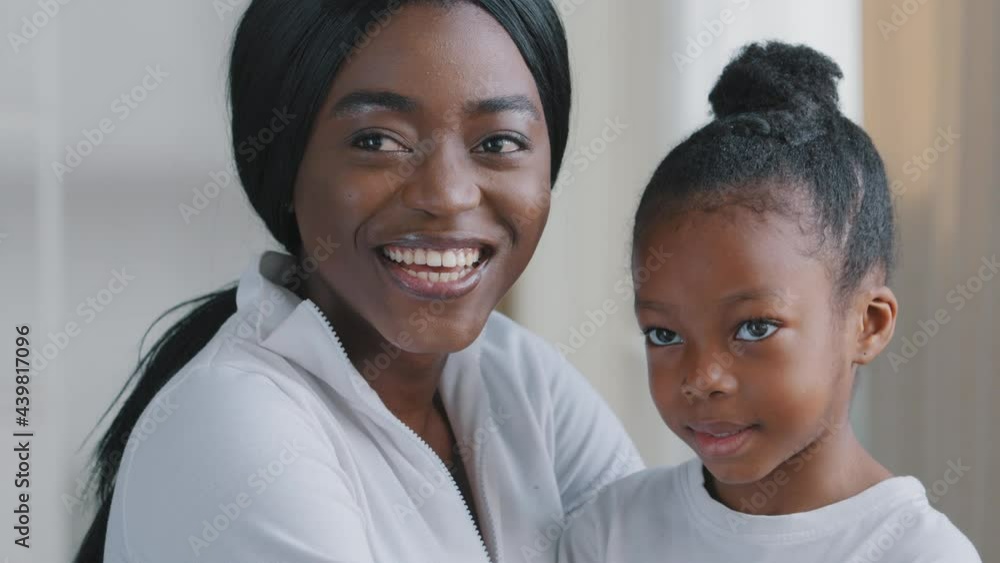 Portrait of happy beautiful african american woman black joyful mother caring afro mommy hugs cuddles little daughter school girl cute child laughs sincerely toothy smiling sitting together indoors Portrait of happy beautiful african american woman black joyful mother caring afro mommy hugs cuddles little daughter school girl cute child laughs sincerely toothy smiling sitting together indoors