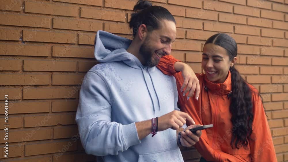 Young friends wearing sports clothes using mobile phone after working out. They are smiling and having fun. Young friends wearing sports clothes using mobile phone after working out. They are smiling and having fun.