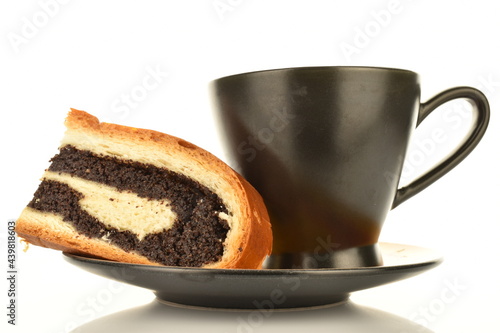 One fragrant freshly baked poppy roll slice on a black saucer with a cup, close-up, isolated on white. photo