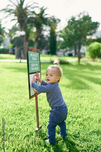 Kid is standing on a green lawn and holding his hands for a sign-pointer