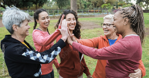 Multiracial women stacking hands outdoor at city park - Main focus on center senior woman face