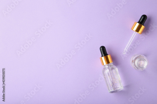 A glass bottles with a pipette with oil, serum on purple background with copy space. Flatlay