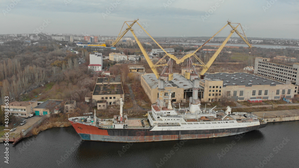 Ariel view of old cargo ship is moored at the dock on the river. There are two cranes nearby. Nikolaev city, Ukraine