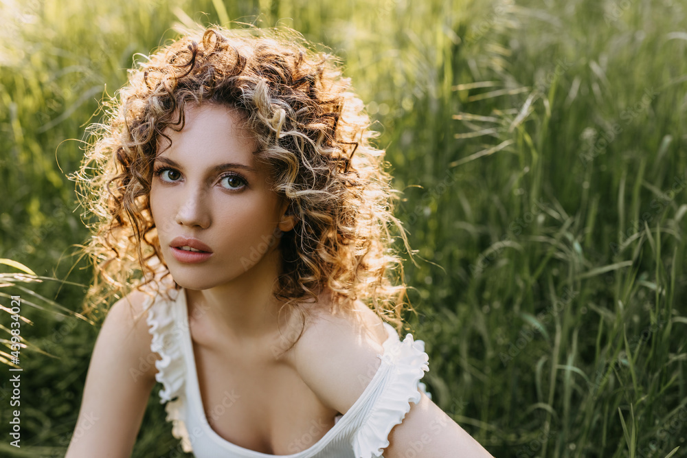Young calm woman with curly hair, sitting in a field with green grass. Young calm woman with curly hair, sitting in a field with green grass.