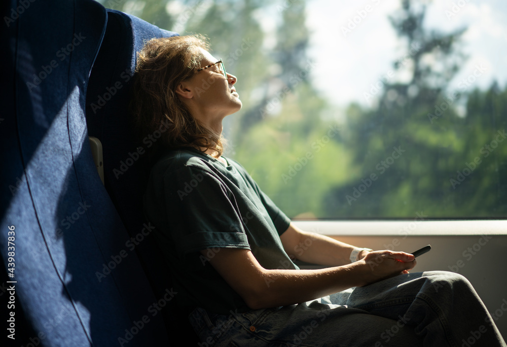 Young beautiful woman wearing glasses sitting in a chair in a high-speed train relaxing while traveling