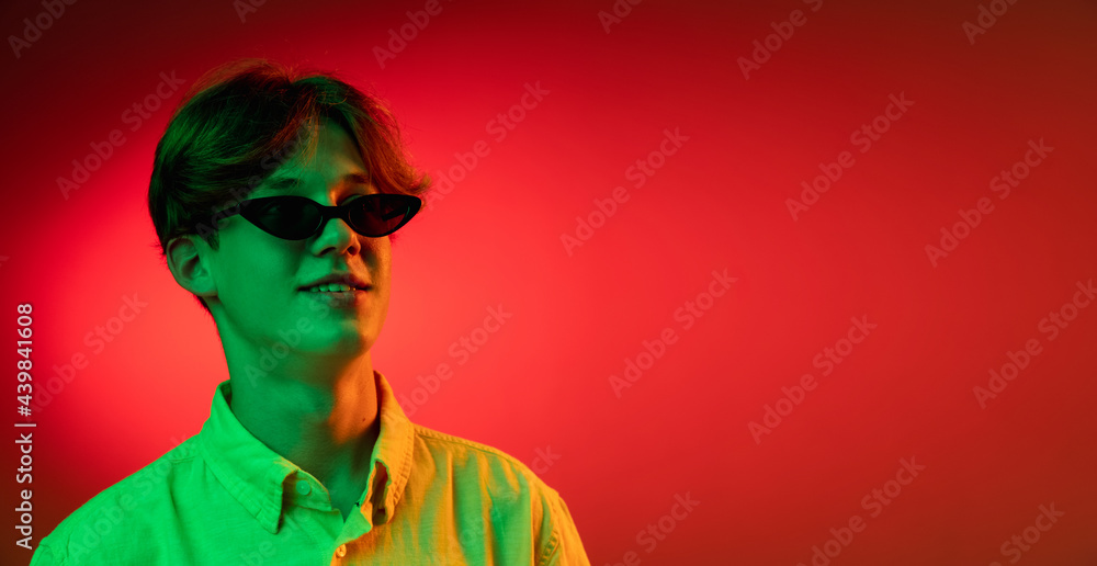 Caucasian young man's portrait on dark studio background in neon. Concept of human emotions, facial expression.