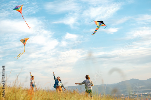 Obraz na plátně Smiling girls and brother boy with flying colorful kites - popular outdoor toy on the high grass mountain meadow