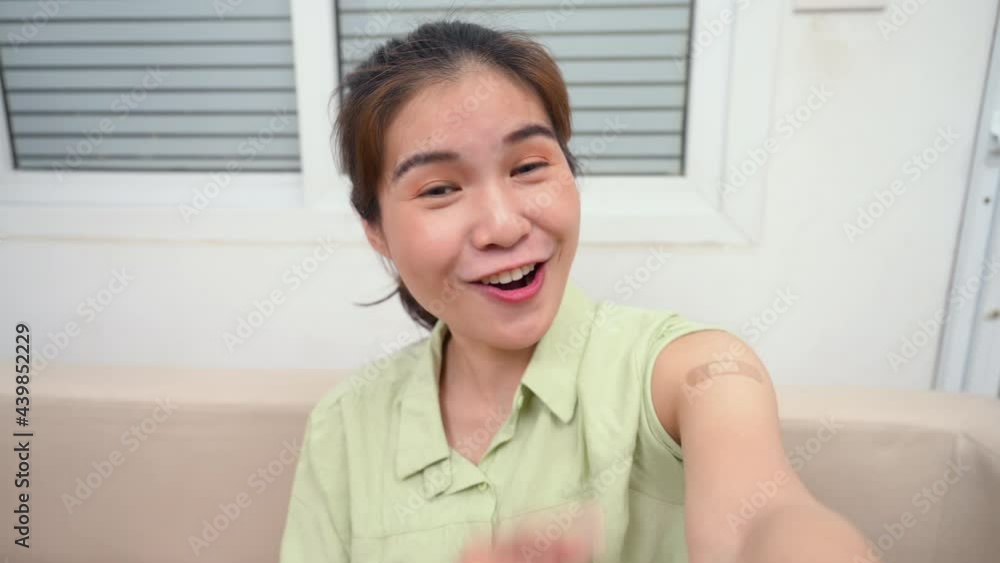 Asian young woman is sitting smiling and talking to camera life streaming by smartphone after vaccination for prevent coronavirus. Happy female making selfie after vaccination and show plaster on arm. Asian young woman is sitting smiling and talking to camera life streaming by smartphone after vaccination for prevent coronavirus. Happy female making selfie after vaccination and show plaster on arm.