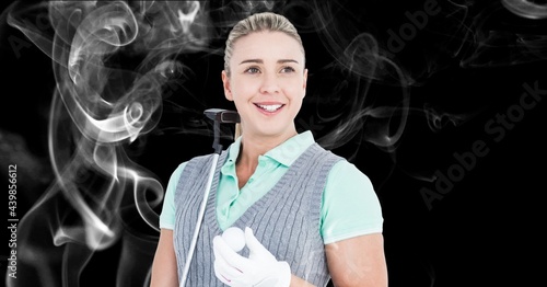Caucasian female golf player holding golf club and ball against smoke effect on black background