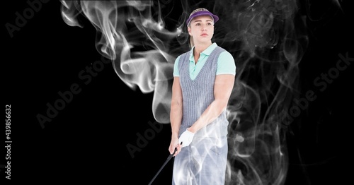 Caucasian female golf player holding golf club against smoke effect on black background