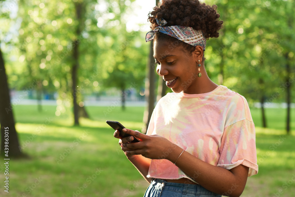African young woman reading a message on mobile phone and smiling while standing outdoors
