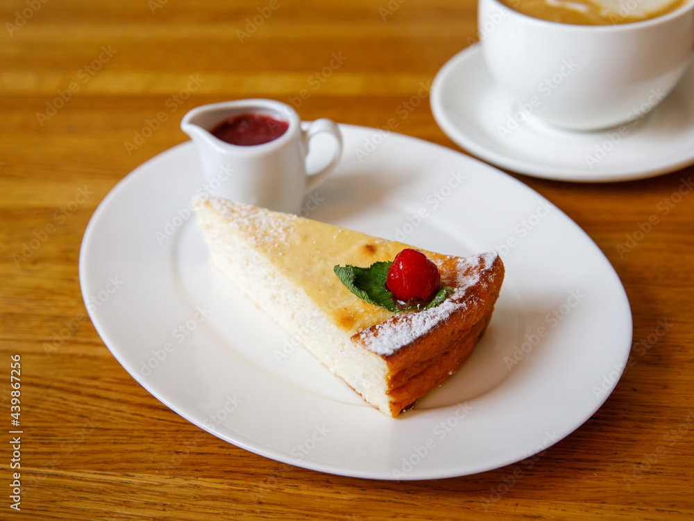 Piece of cheese casserole or cheesecake, garnished with raspberry jam and cup cappuccino coffee on wooden table. Breakfast in cafe, top view, horizontal Traditional russian ukrainian breakfast Piece of cheese casserole or cheesecake, garnished with raspberry jam and cup cappuccino coffee on wooden table. Breakfast in cafe, top view, horizontal Traditional russian ukrainian breakfast