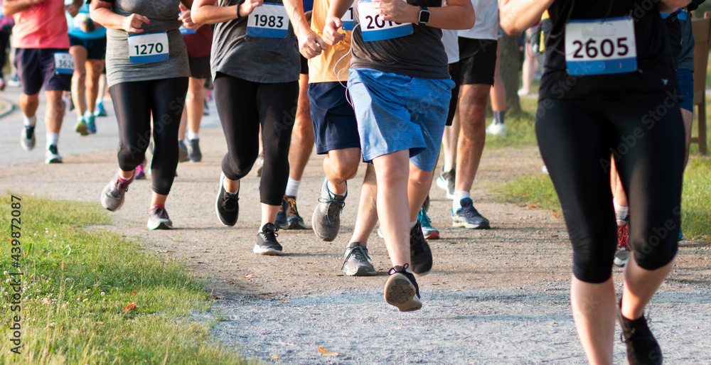 Runners in a crowded race running a 5K around a lake on a dirt trail in a park Runners in a crowded race running a 5K around a lake on a dirt trail in a park