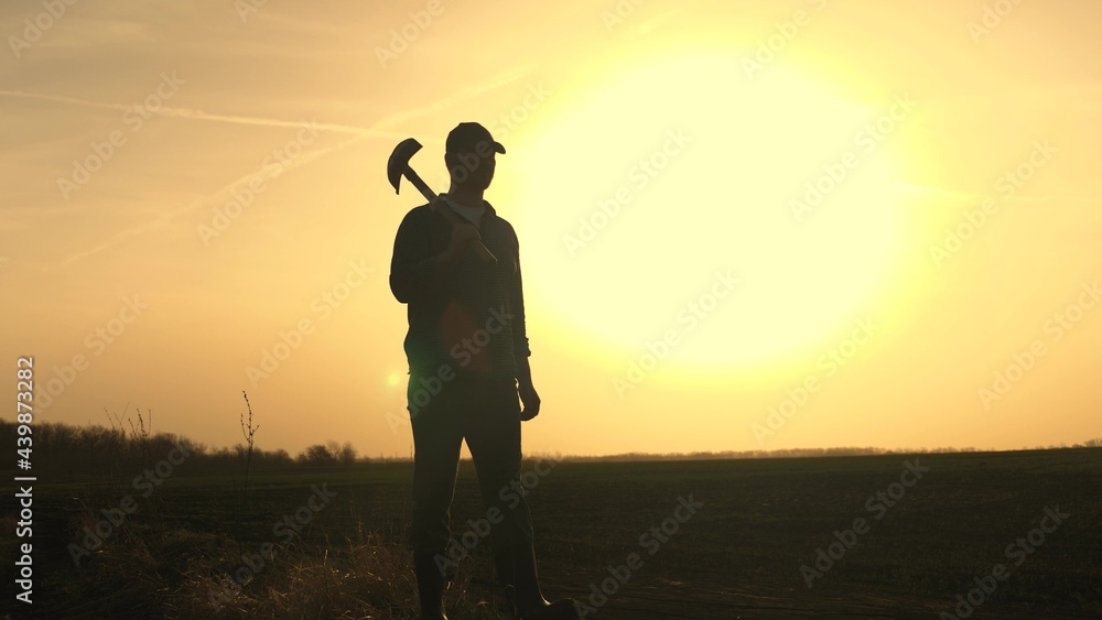 A farmer walks through the field with a shovel in rubber boots to dig the soil of the land at sunset, agriculture, land, growing vegetables, berries and fruits, planting seedlings, digging season