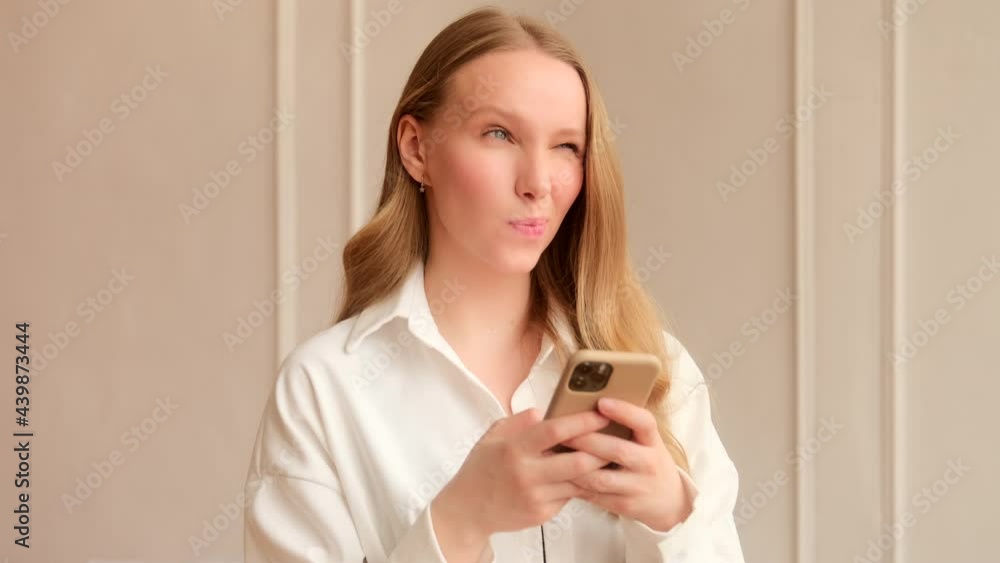 Young woman pensively thinks having doubts and using a mobile phone, chatting in social media texting online with friends through a messenger, plays mobile games app. Young woman pensively thinks having doubts and using a mobile phone, chatting in social media texting online with friends through a messenger, plays mobile games app.