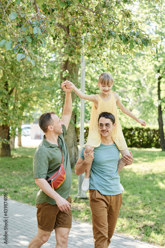 Happy gay couple walking with their daughter together in the park