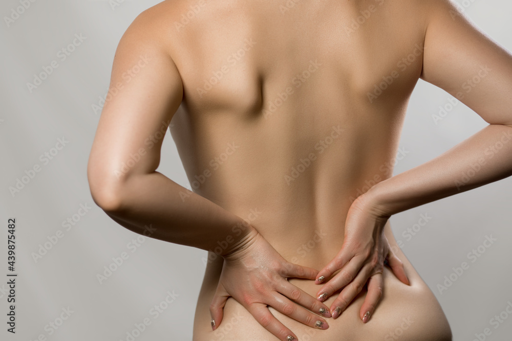 Woman having backache, pain back isolated on gray background. Scoliosis. Spinal cord problems on womans back. Beautiful naked woman touching her back.