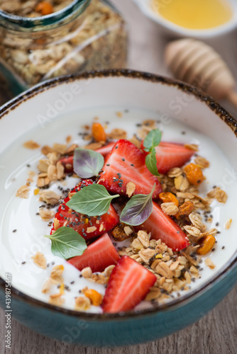 Close-up of yogurt topped with granola and strawberry and served in a turquoise bowl, selective focus