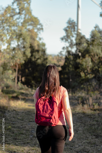 vertical shot of a young latina with red backpack walking in the middle of nature practicing trekking. Concept of good health through sport and recreation. © Fabrizio