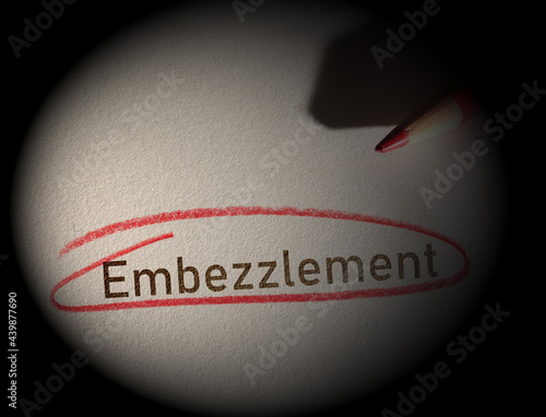 Embezzlement text circled in red pencil on dark background photo