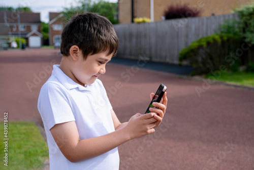 Portrait schoolboy using smartphone typing text messages, Happy kid standing outdoor using cellphone chatting with friends,Child boy sending texts via mobilephone. Children with social network concept