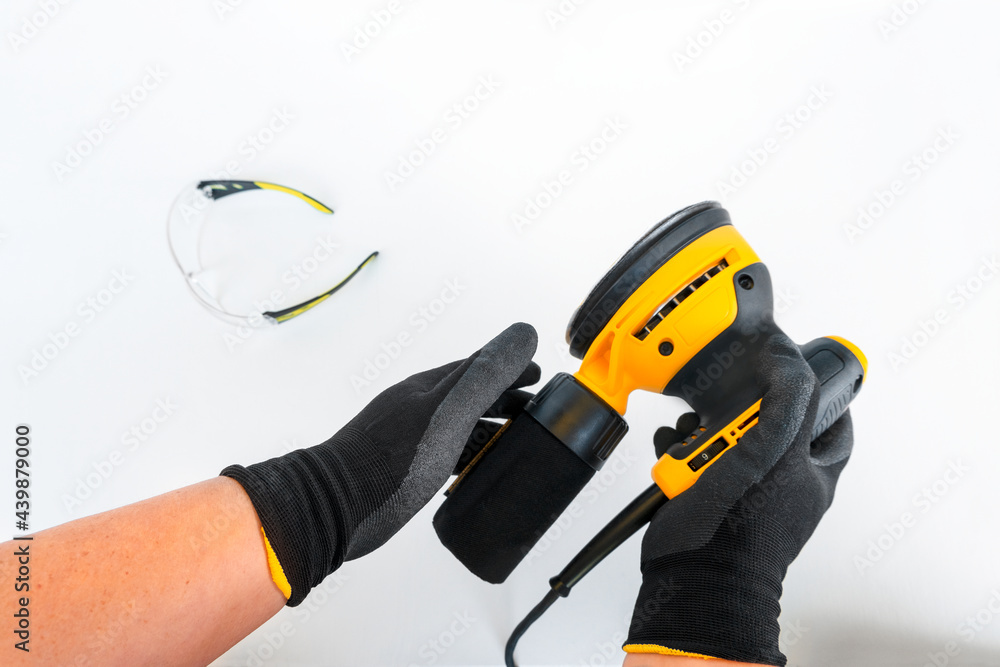 Circular electric power sander,grinder tool,surface sanding machine with container for collecting dust in strong male hands,blurred protection goggles on white background,horizontal banner,copy space Circular electric power sander,grinder tool,surface sanding machine with container for collecting dust in strong male hands,blurred protection goggles on white background,horizontal banner,copy space