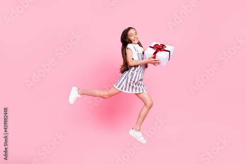 Full length body size photo schoolgirl jumping high careless giving present at party isolated pastel pink color background © deagreez