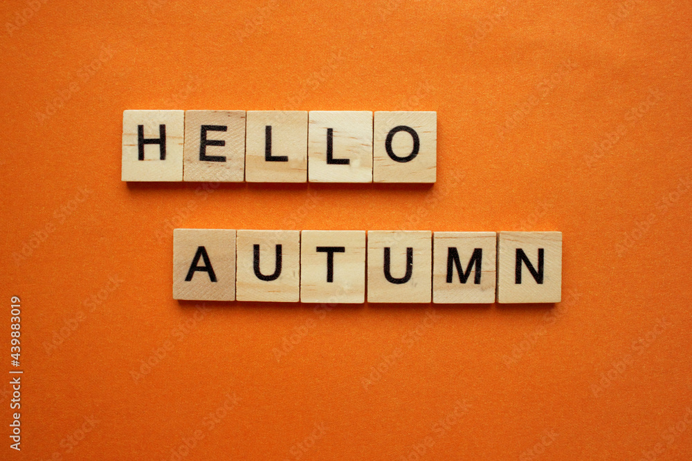 Obraz premium The word Hello Autumn is made of wooden cubes on an orange background. The word is on top. The concept of a cozy autumn mood. Cope space. View from above