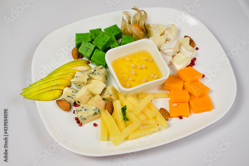 Cheese variety board or platter with cheese assortment, grapes, honey and nuts. Black stone background. Top view, flat lay