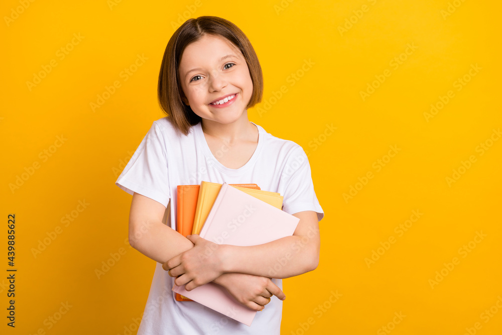 Photo of sweet pretty school girl wear white t-shirt smiling hugging book stack isolated yellow color background Photo of sweet pretty school girl wear white t-shirt smiling hugging book stack isolated yellow color background