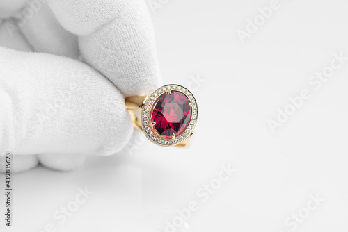 Golden ring with rhodolite gem and diamonds in jeweler hand in a white glove photo