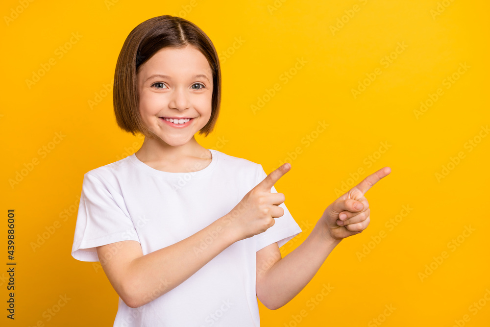 Photo of charming sweet school girl wear white t-shirt smiling pointing two fingers empty space isolated yellow color background Photo of charming sweet school girl wear white t-shirt smiling pointing two fingers empty space isolated yellow color background