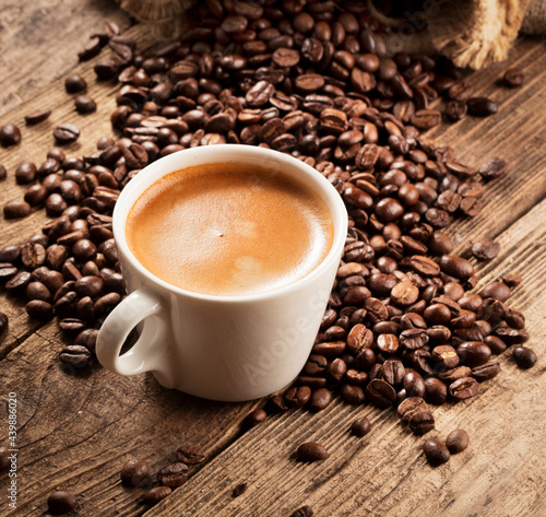 heap of coffee beans with cup of fresh coffee on wooden background